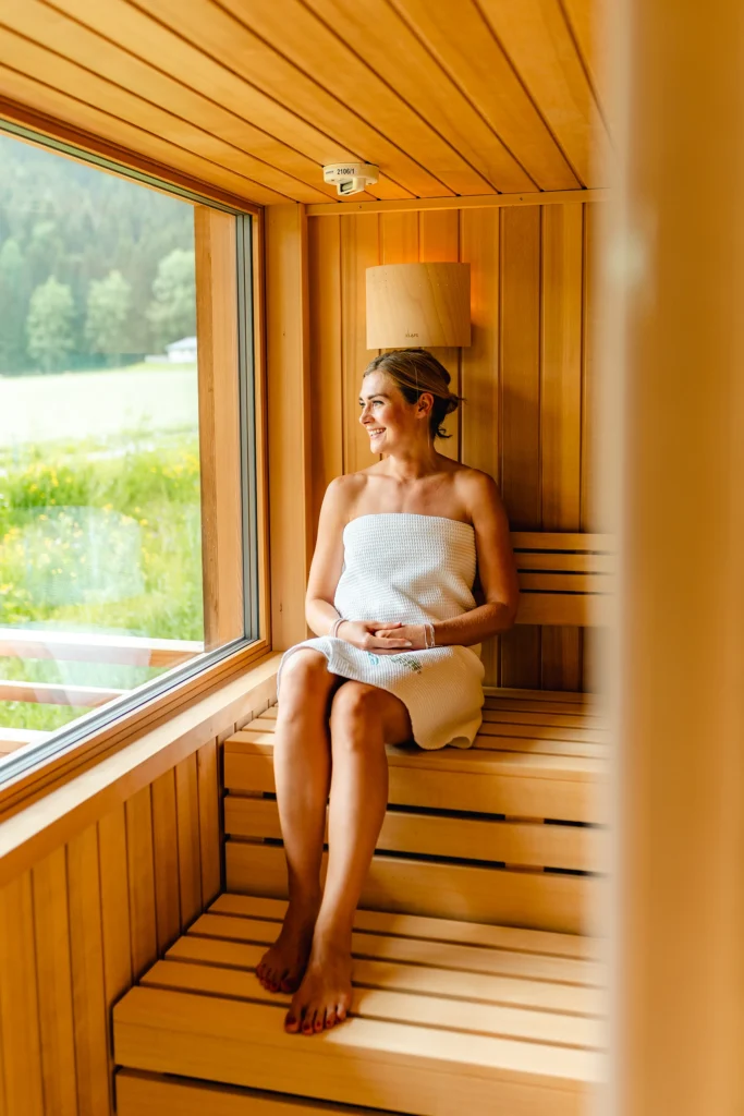 Wo Urlaub auf Natur trifft durften durften wir dieses Foto im Das Leonhard Naturparkhotel in der Sauna aufnehmen. Es zeigt eine Dame die in der Sauna sitzt und auf die grüne Wiese hinaus blickt. Werbeagnetur SquadTwenty gmbH Kärnten Tourismusfotografie und Contentcreation