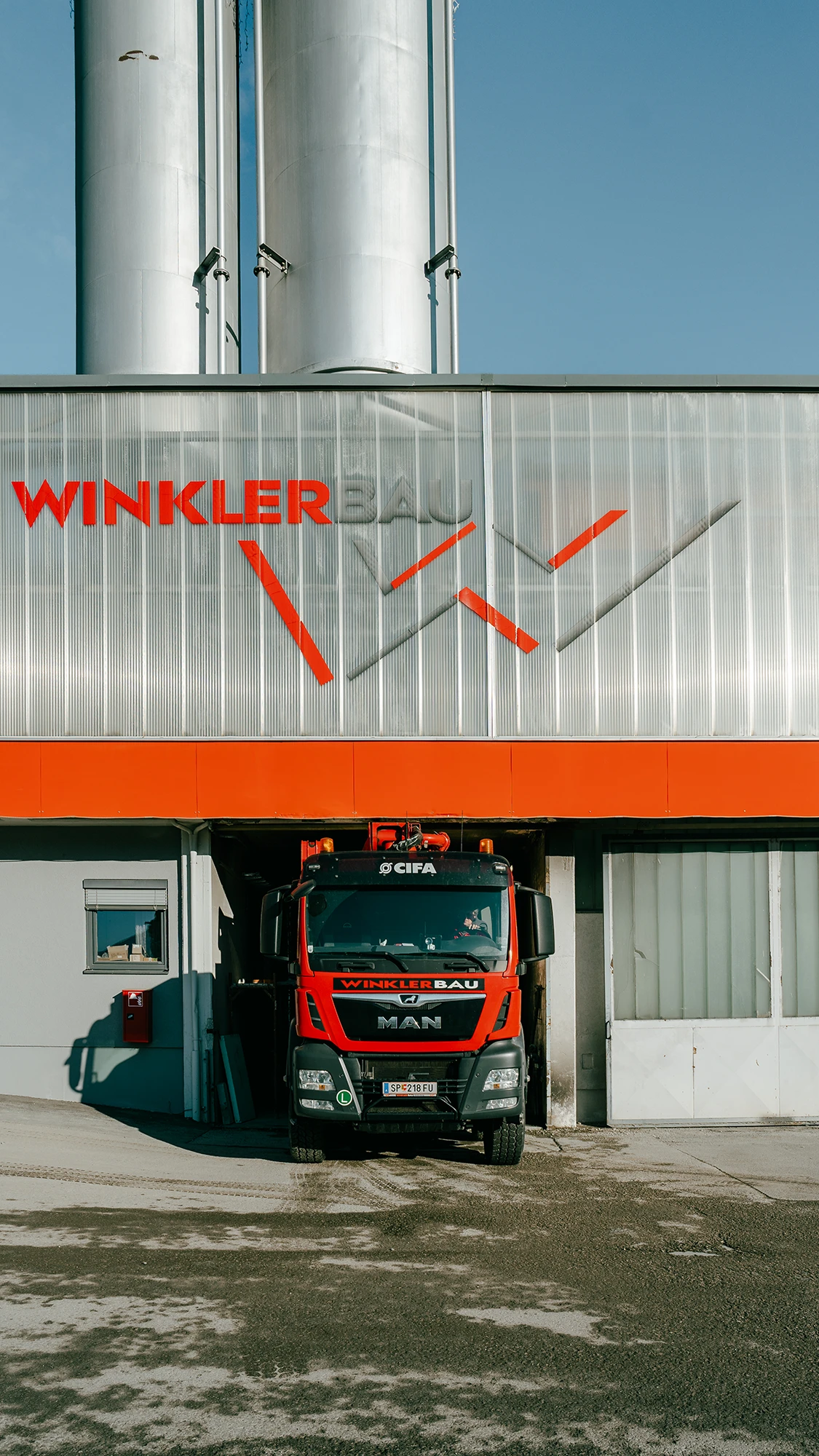 Zu sehen ist das Mischwerk der Firma WinklerBau in Greifenburg mit einem LKW in der Ladezone darunter.
