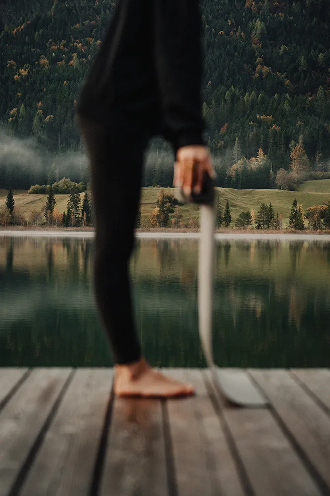 Barfuß auf einem Steg am See, eine Yogamatte in der Hand. Hatha Harmony Yoga – SquadTwenty Werbeagentur Kärnten