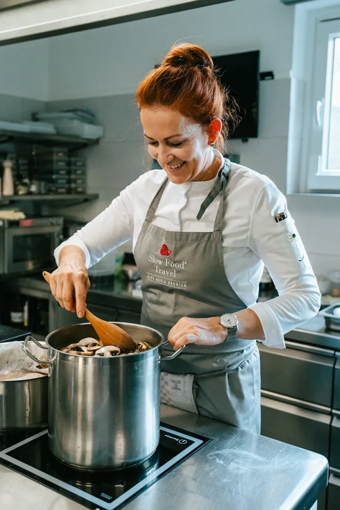 In einer eleganten Profiküche stellt eine Frau in einer grauen Schürze schmackhafte Pilzinhalte für die dynamische Social-Media-Kampagne von SquadTwenty her. – SquadTwenty Werbeagentur Kärnten