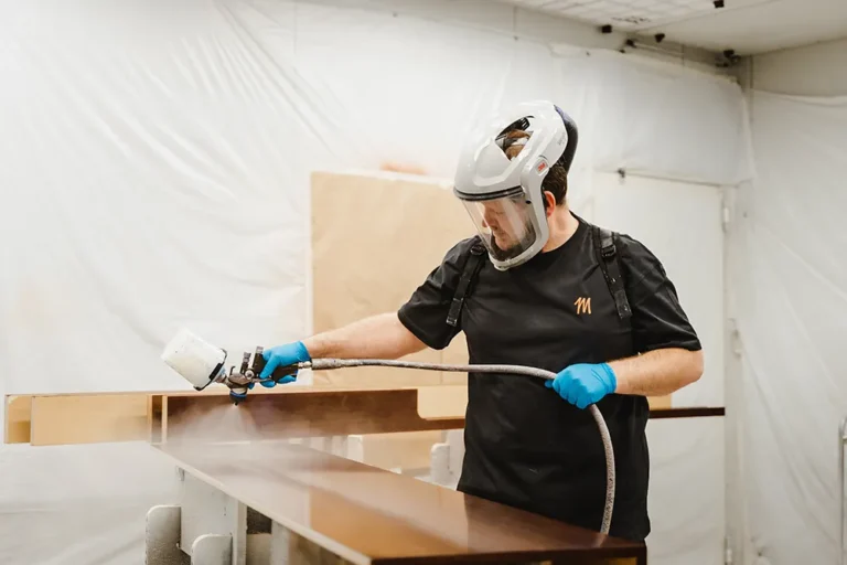 Ein SquadTwenty-Teammitglied in Schutzkleidung lackiert fachmännisch Holz in unserer dynamischen, innovationsgetriebenen Werkstatt. – SquadTwenty Werbeagentur Kärnten