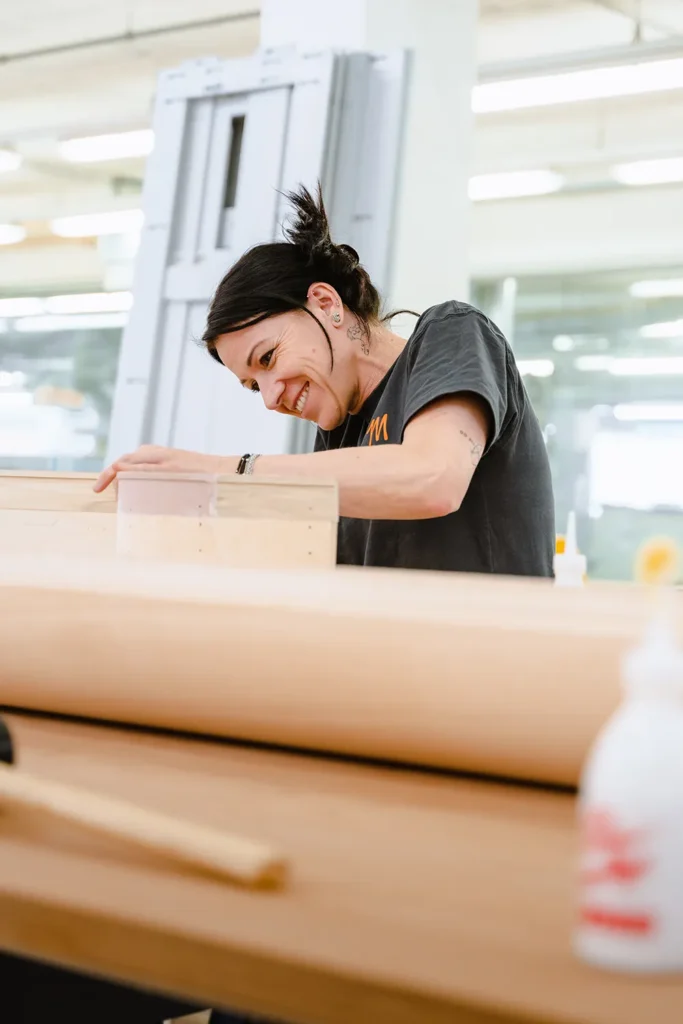 Ein tätowierter Kreativer fertigt in einem sonnendurchfluteten Studio ein Holzprojekt an, das den kühnen, innovativen Ansatz von SquadTwenty in Sachen Markendesign verkörpert. – SquadTwenty Werbeagentur Kärnten