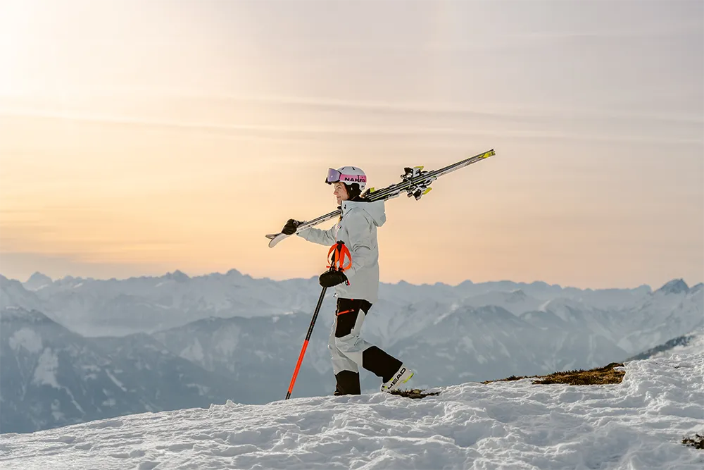 Die Farben des Sonnenuntergangs umrahmen einen Skifahrer in Bewegung, der mit Skiern und Stöcken in der Hand über verschneite Gipfel wandert - Abenteuer pur, bereit für die Geschichte Ihrer Marke. – SquadTwenty Werbeagentur Kärnten