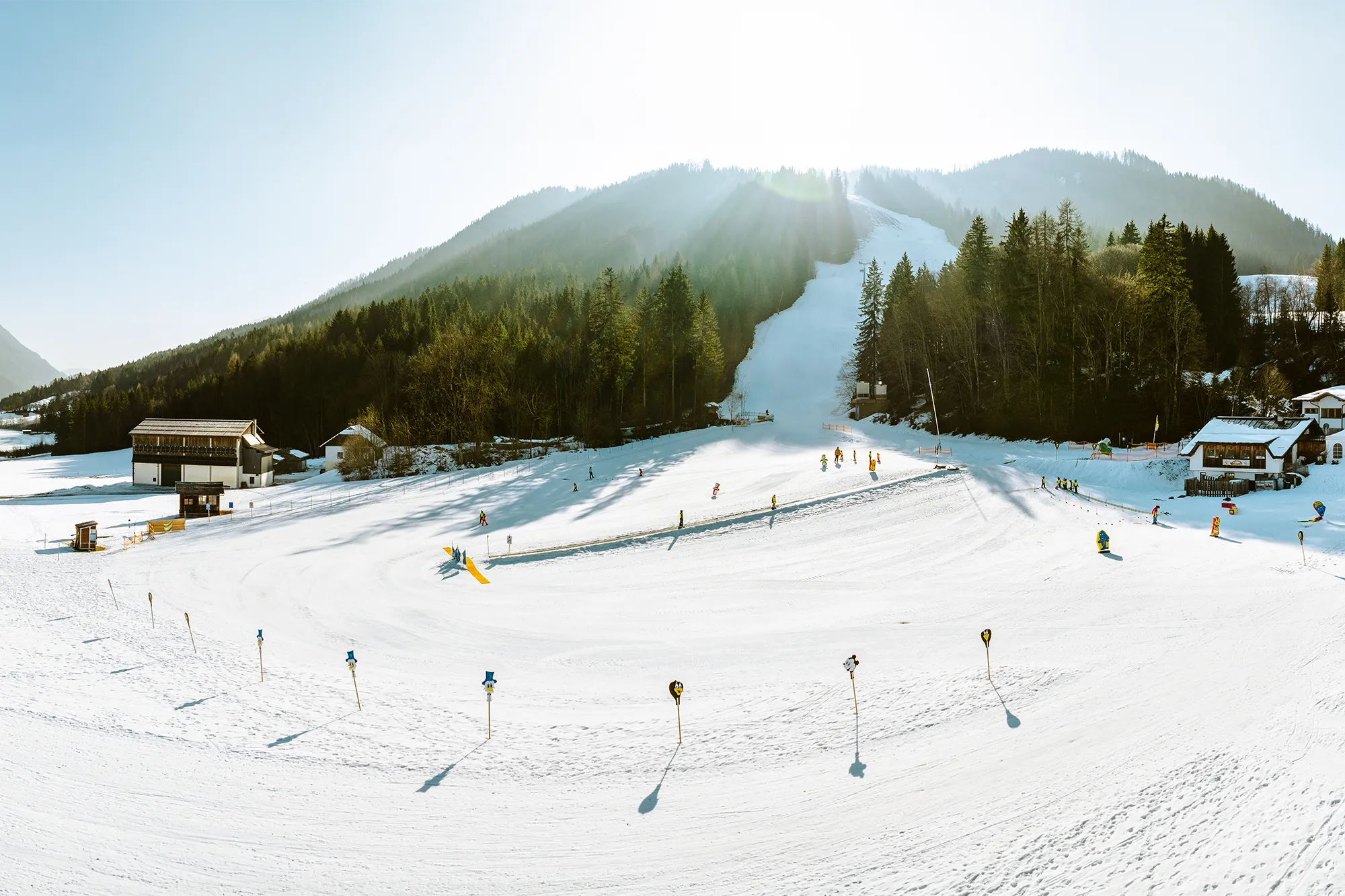Eine unberührte Skipiste mit aktiven Skifahrern, gemütlichen Chalets und sonnenbeschienenen Waldhügeln - ein ideales Bild für herausragende SquadTwenty-Kampagnen. – SquadTwenty Werbeagentur Kärnten