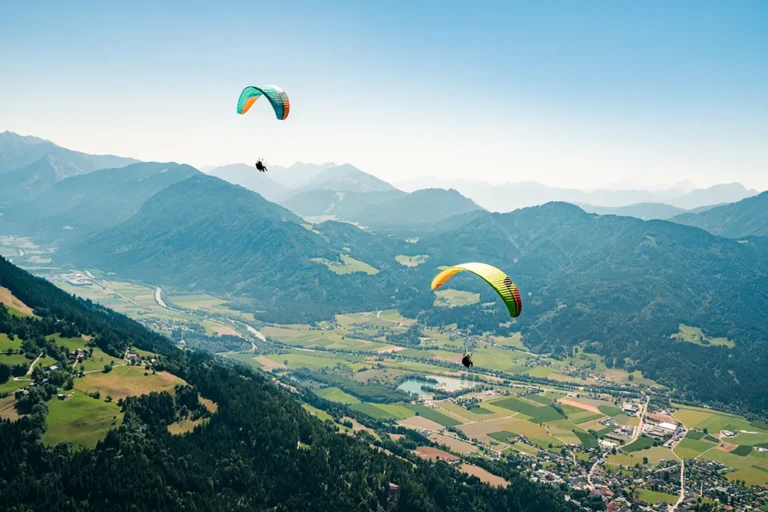Ein dynamisches Duo beim Gleitschirmfliegen über üppigen Tälern und einer pulsierenden Stadt - ideal für erstklassige Inhalte und herausragende Social-Media-Kampagnen. – SquadTwenty Werbeagentur Kärnten