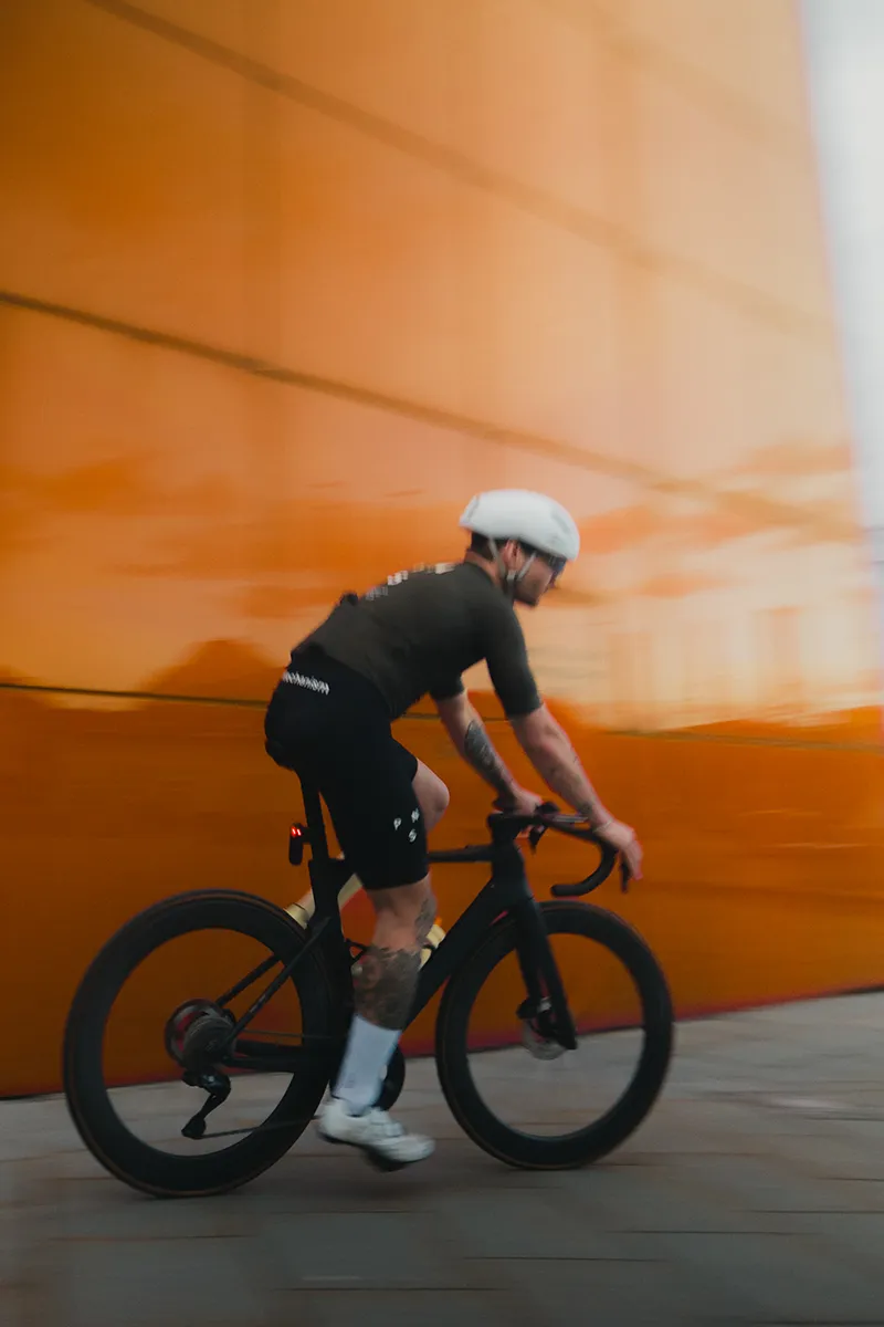 Ein eleganter Radfahrer in schwarzer Sportkleidung und Helm macht Kontakt mit einer auffälligen orangefarbenen Wand und fängt Bewegung und kühne urbane Energie ein. – SquadTwenty Werbeagentur Kärnten