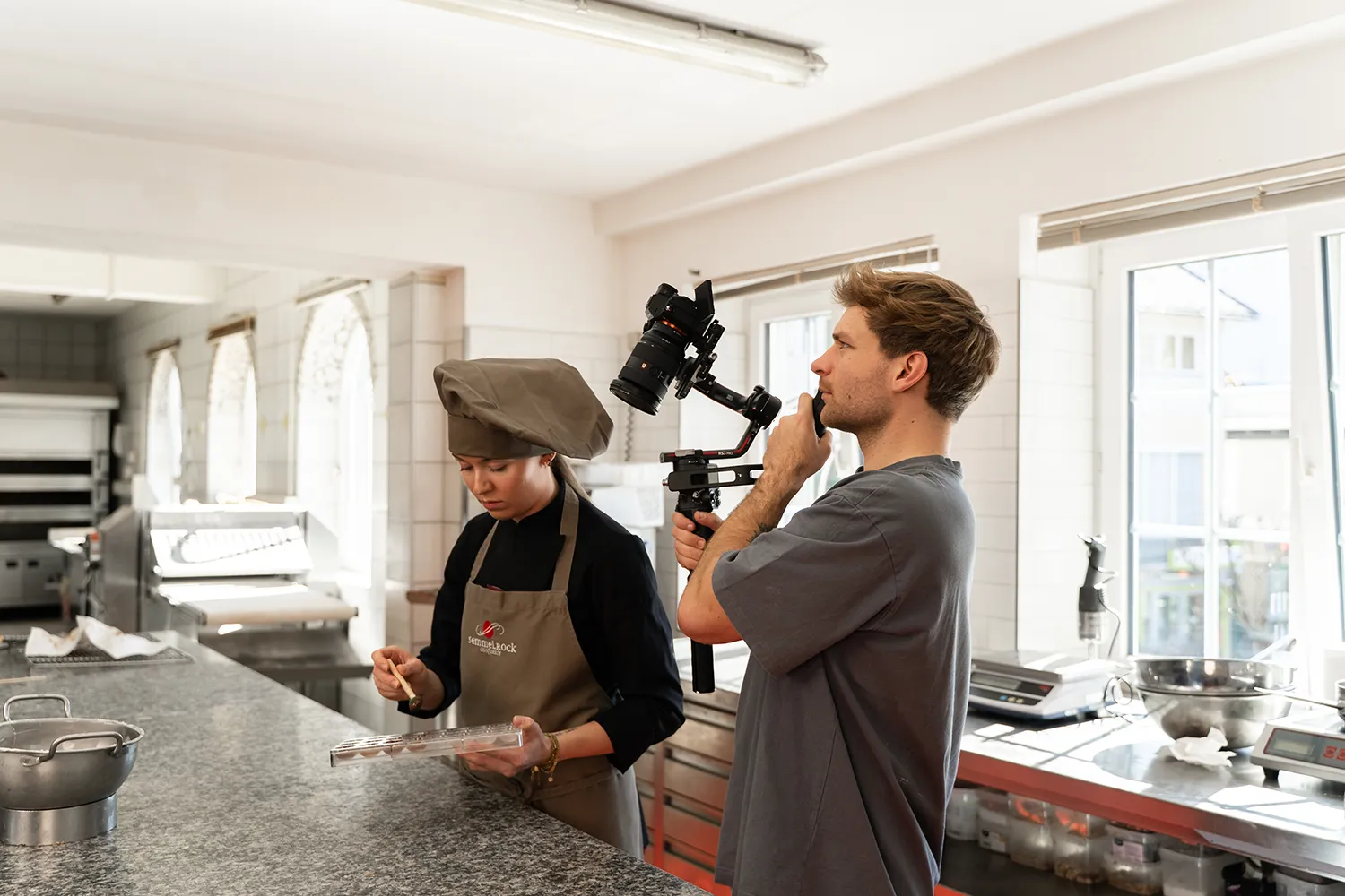 In einer eleganten, modernen Küche fängt ein Filmemacher einen Koch bei der Zubereitung von Speisen ein - und wirft damit ein Schlaglicht auf die dynamische Erstellung von Inhalten für Social Storytelling. – SquadTwenty Werbeagentur Kärnten