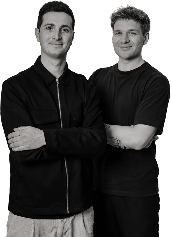 Zwei Kreative von SquadTwenty stehen selbstbewusst beieinander, lächelnd, die Arme verschränkt, die Hände entspannt - und verkörpern die Synergie von Inhalt und Design. – SquadTwenty Werbeagentur Kärnten